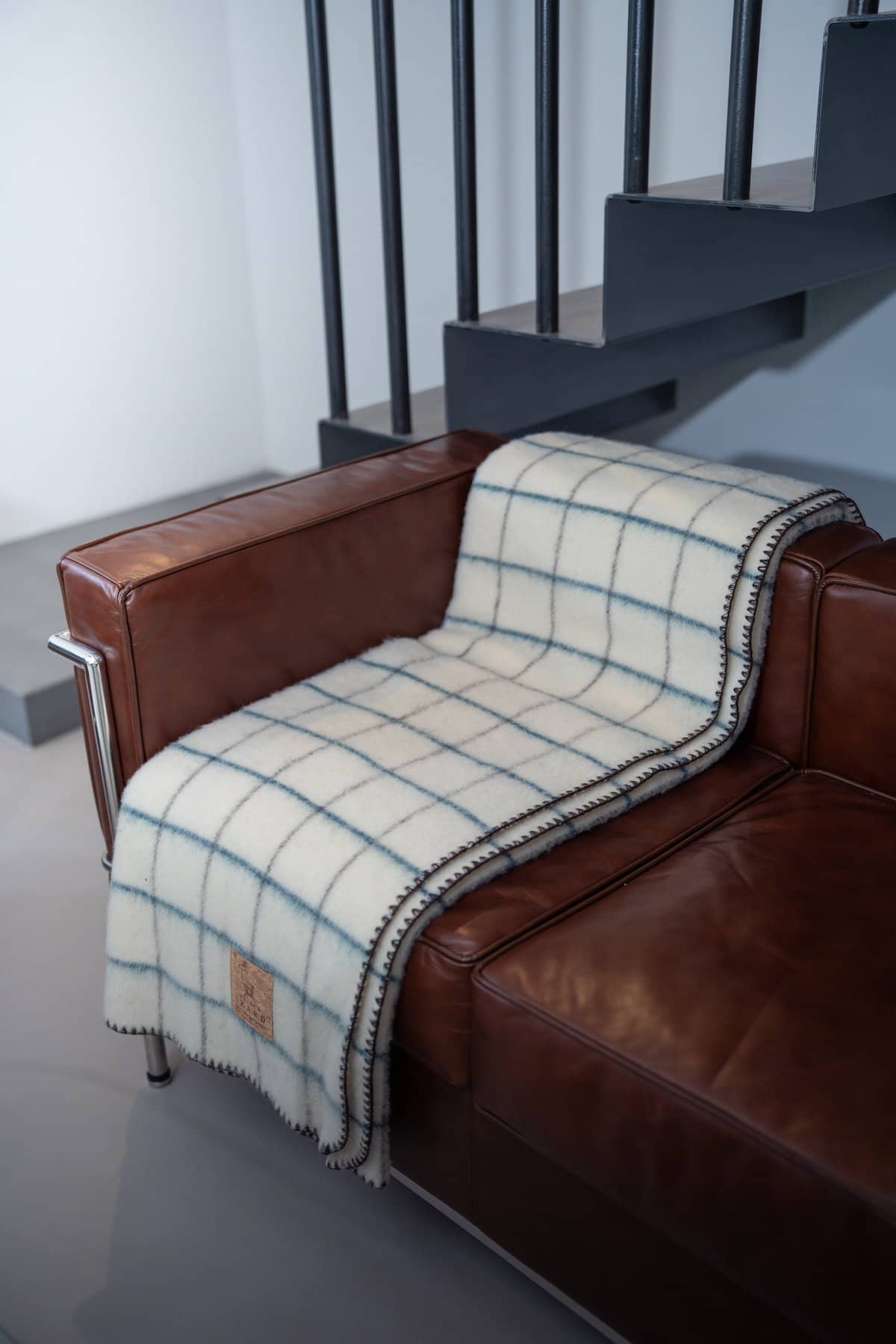 Plaid Calou laine française écru à carreaux bleu paon et marron posé sur un fauteuil