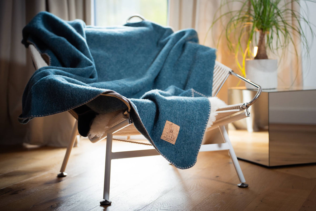 Plaid bleu paon en laine française Calou posé sur un fauteuil